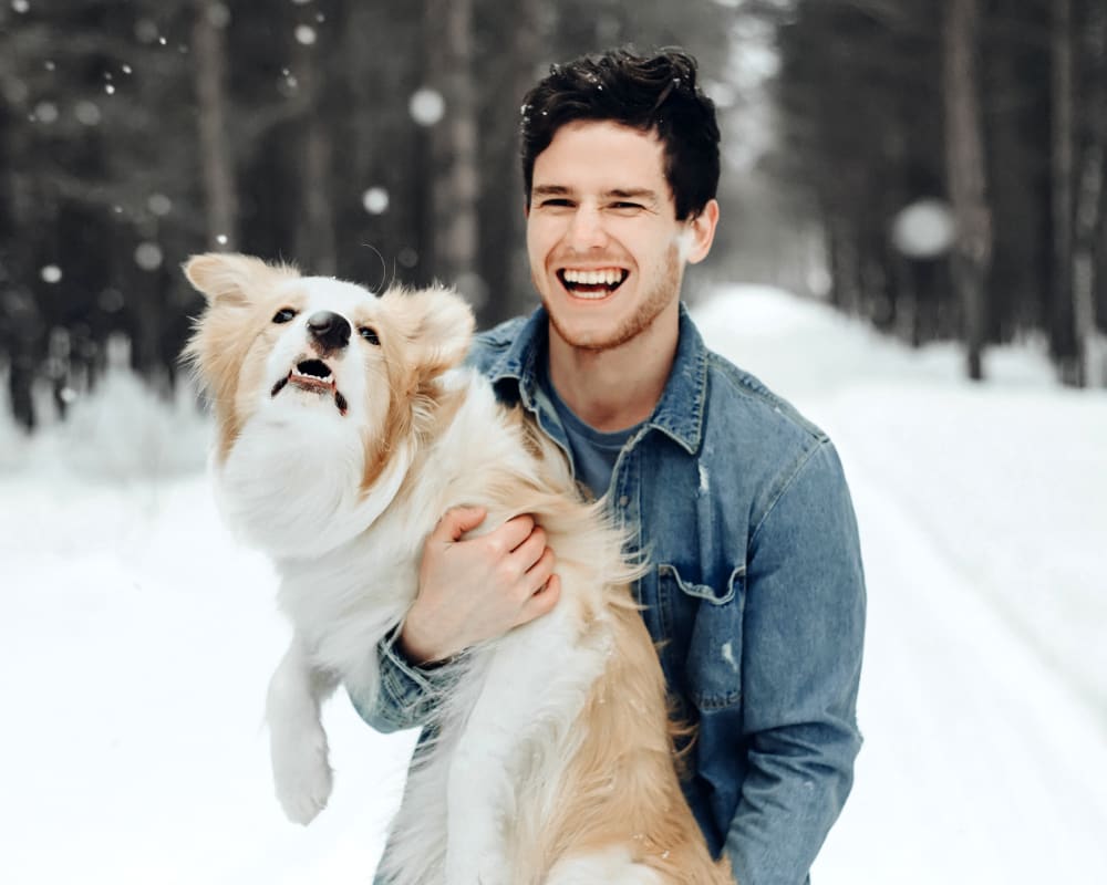 A man and a fluffy white and beige dog play in the snow outside.