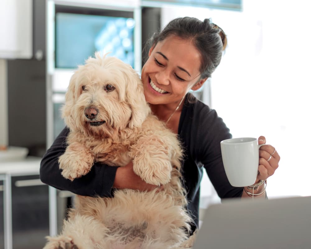 A woman holds a fluffy beige dog up while holding a mug in the other hand.